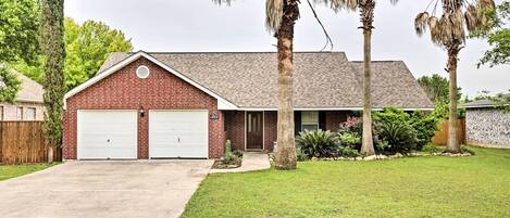 A single-story brick house with two attached garages, a front lawn, and mature trees.