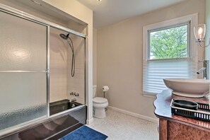 Une salle de bain avec une douche à parois de verre, des toilettes blanches, un lavabo avec un grand bac et une fenêtre avec des stores.