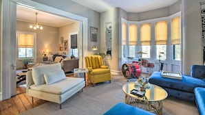 A spacious living room with a sofa, armchair, and coffee table, a drum set, and large windows with blinds. - Walk to Downtown: Pet-friendly Millerton Home! (Millerton)