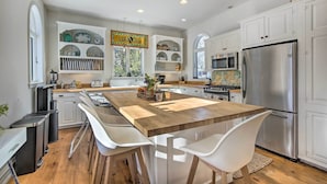 A modern kitchen with white cabinetry, stainless steel appliances, and a wooden island with bar stools. - Walk to Downtown: Pet-friendly Millerton Home! (Millerton)