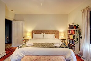 A neatly arranged bedroom with a large bed, bedside lamps, a bookshelf, and a door leading to another room. - Walk to Downtown: Pet-friendly Millerton Home! (Millerton)