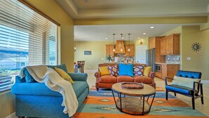 A spacious living room with a blue sofa, a coffee table, and a view through large windows. - La Verkin Home w/ Hot Tub, Kayaks, & Bikes! (La Verkin)