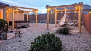 A backyard with a hot tub, wooden pergolas with string lights, a hammock, and a patio area with a table and chairs. - La Verkin Home w/ Hot Tub, Kayaks, & Bikes! (La Verkin)