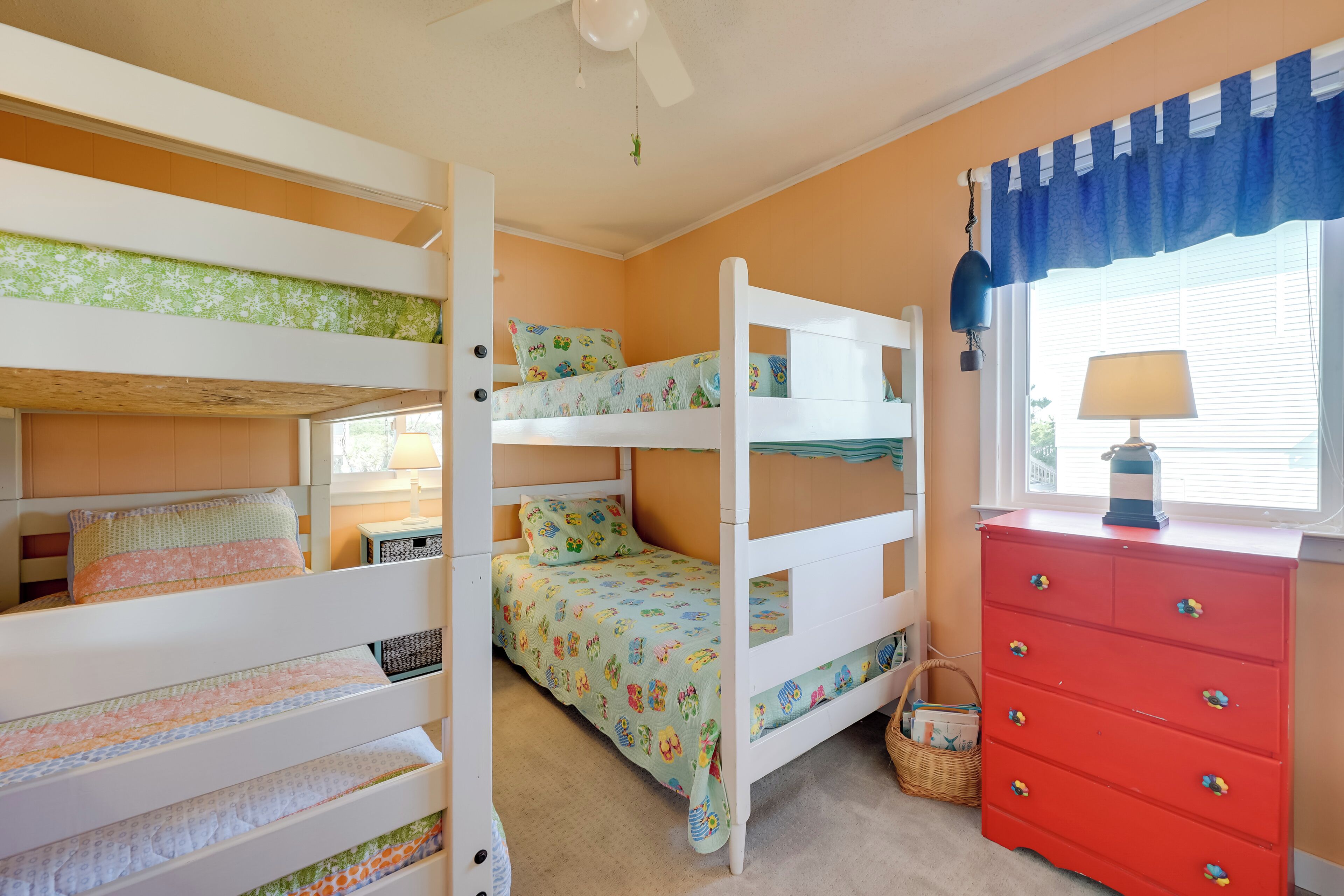 A bunk bed room with a red dresser and a window with curtains.