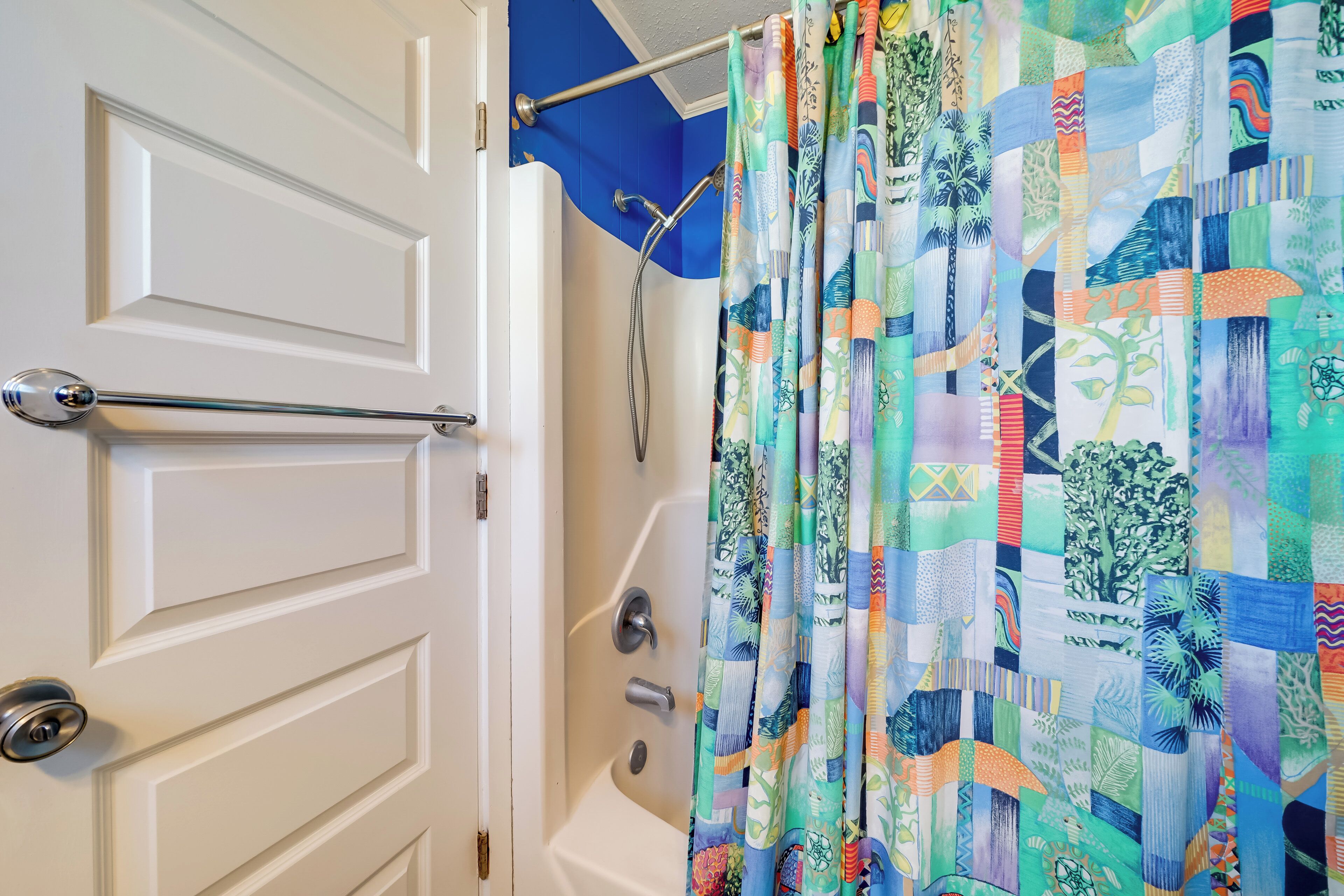 A bathroom with a shower curtain featuring a patchwork design, a white door with a silver handle, and a visible shower head.