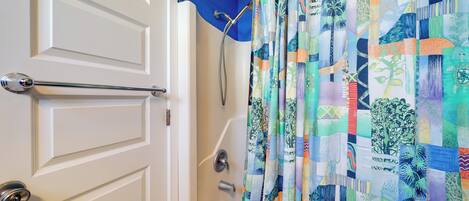 A bathroom with a shower curtain featuring a patchwork design, a white door with a silver handle, and a visible shower head.