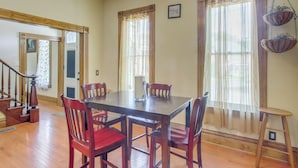 Un coin repas avec une table et des chaises en bois, un escalier et de grandes fenêtres avec des rideaux.