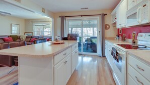 A modern kitchen with a central island, white cabinetry, and a sliding glass door leading to a patio. - Lake Cumberland Resort Condo w/ Direct Lake Access (Bronston)