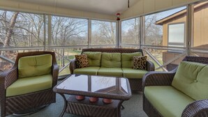 A sunroom with wicker furniture, a glass table, and a view of trees and a house. - Lake Cumberland Resort Condo w/ Direct Lake Access (Bronston)