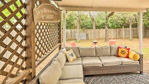A covered outdoor seating area with a wicker sofa, a 'Welcome Y'all' sign, and a wooden lattice fence. - Fort Worth Retreat w/ Fenced Yard & Fire Pit! (Fort Worth)