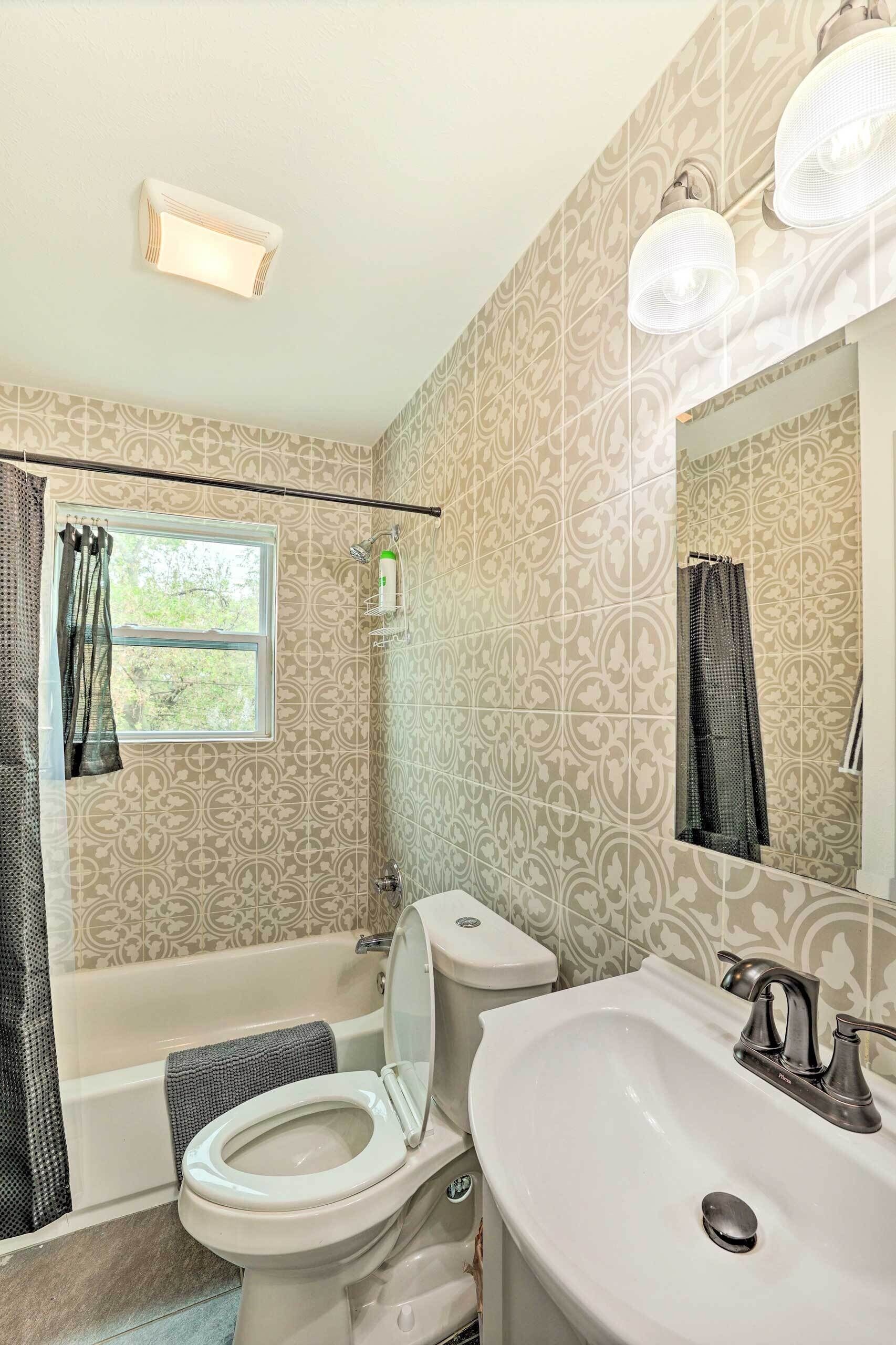 A bathroom with a toilet, sink, and bathtub. There is a window with a curtain, and a shower curtain is visible.