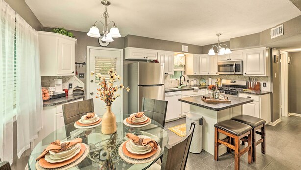 A modern kitchen with white cabinets, stainless steel appliances, and a glass dining table set for four. - Fort Worth Retreat w/ Fenced Yard & Fire Pit! (Fort Worth)
