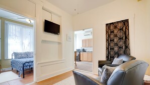 Ein modernes Wohnzimmer mit einer Couch, einem an der Wand befestigten Fernseher und Blick in den Küchenbereich.