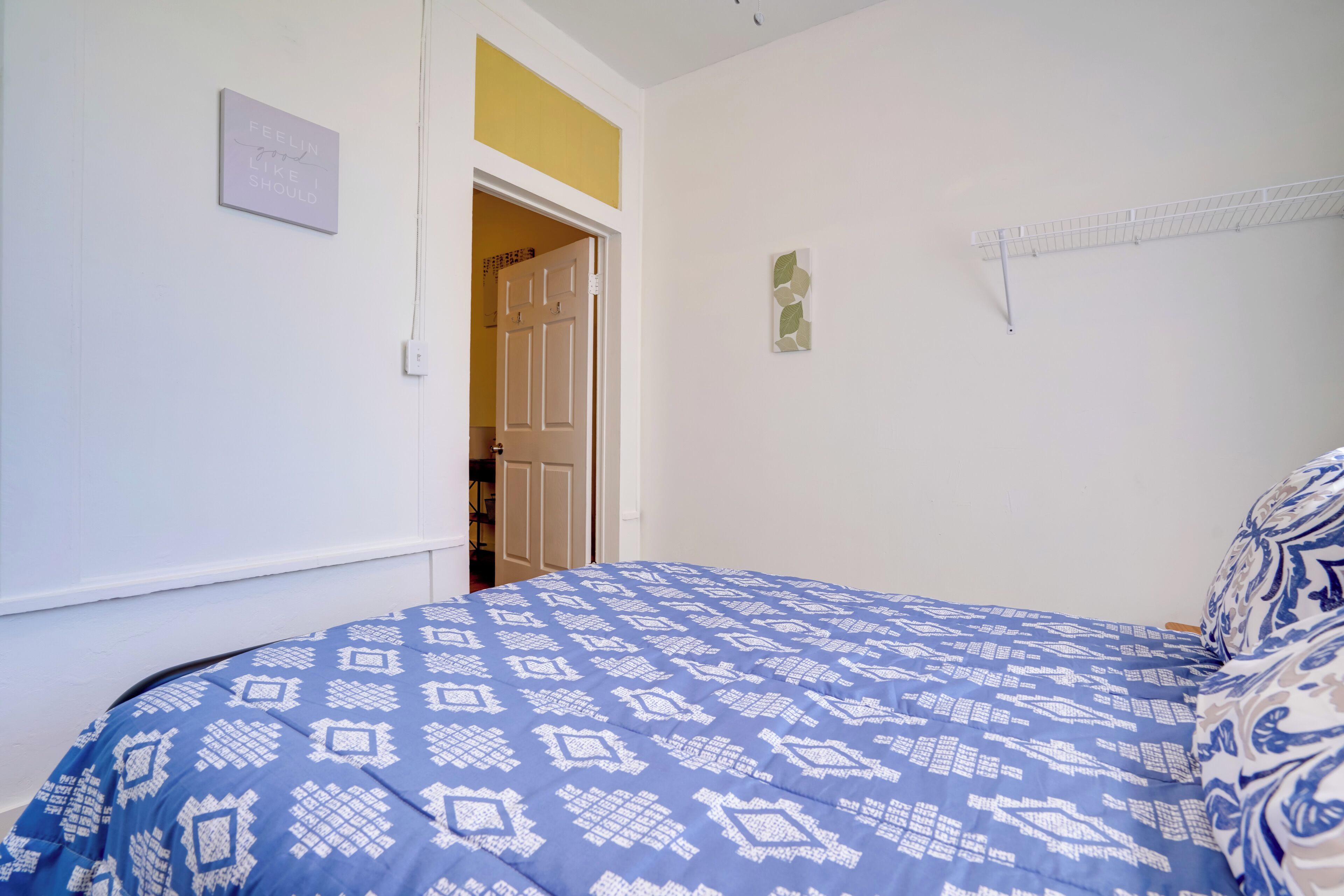 A bedroom with a blue patterned bedspread, a white door, and a wall-mounted shelf.
