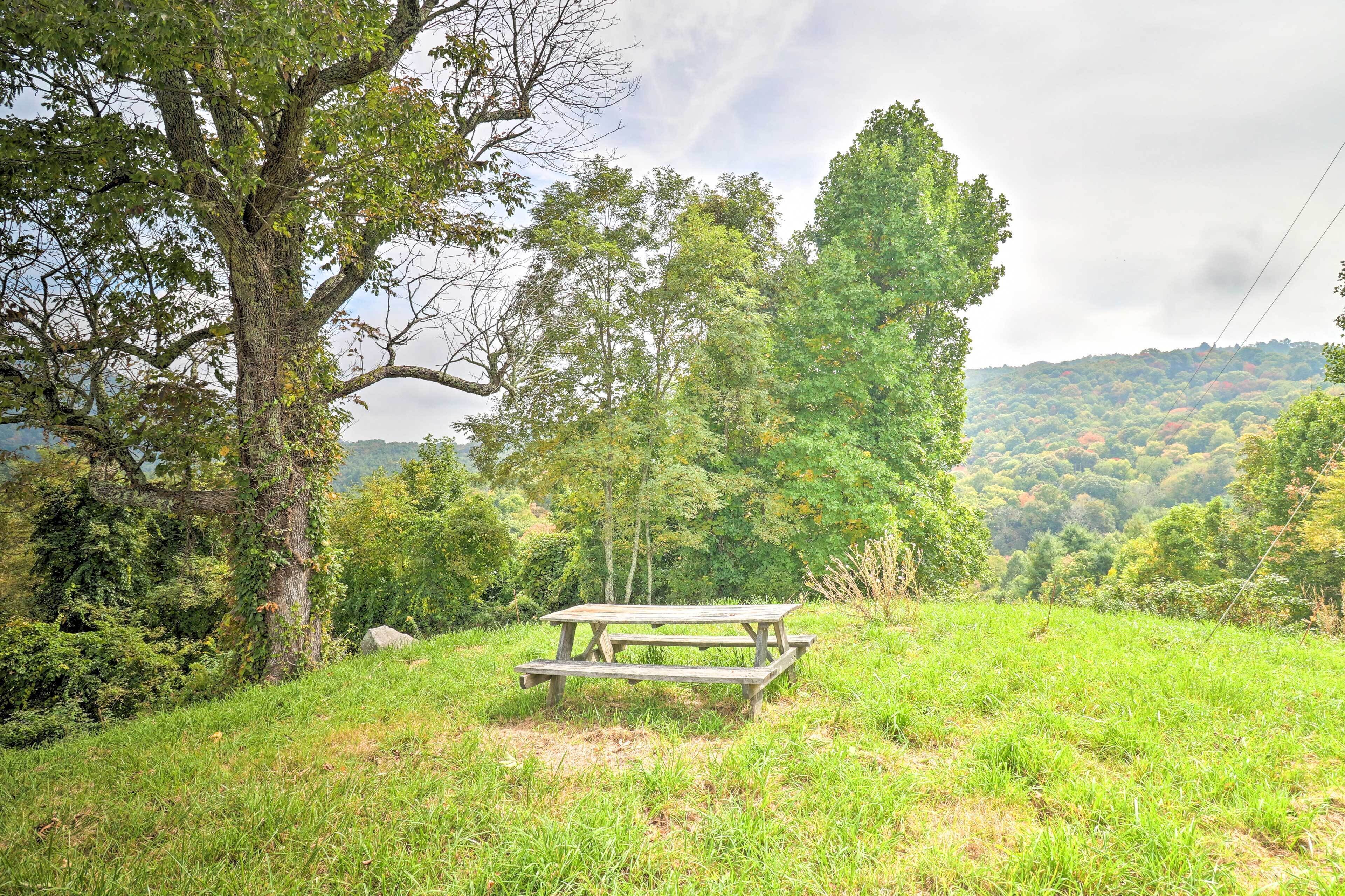 A picnic table in a grassy area with trees and hills in the background.