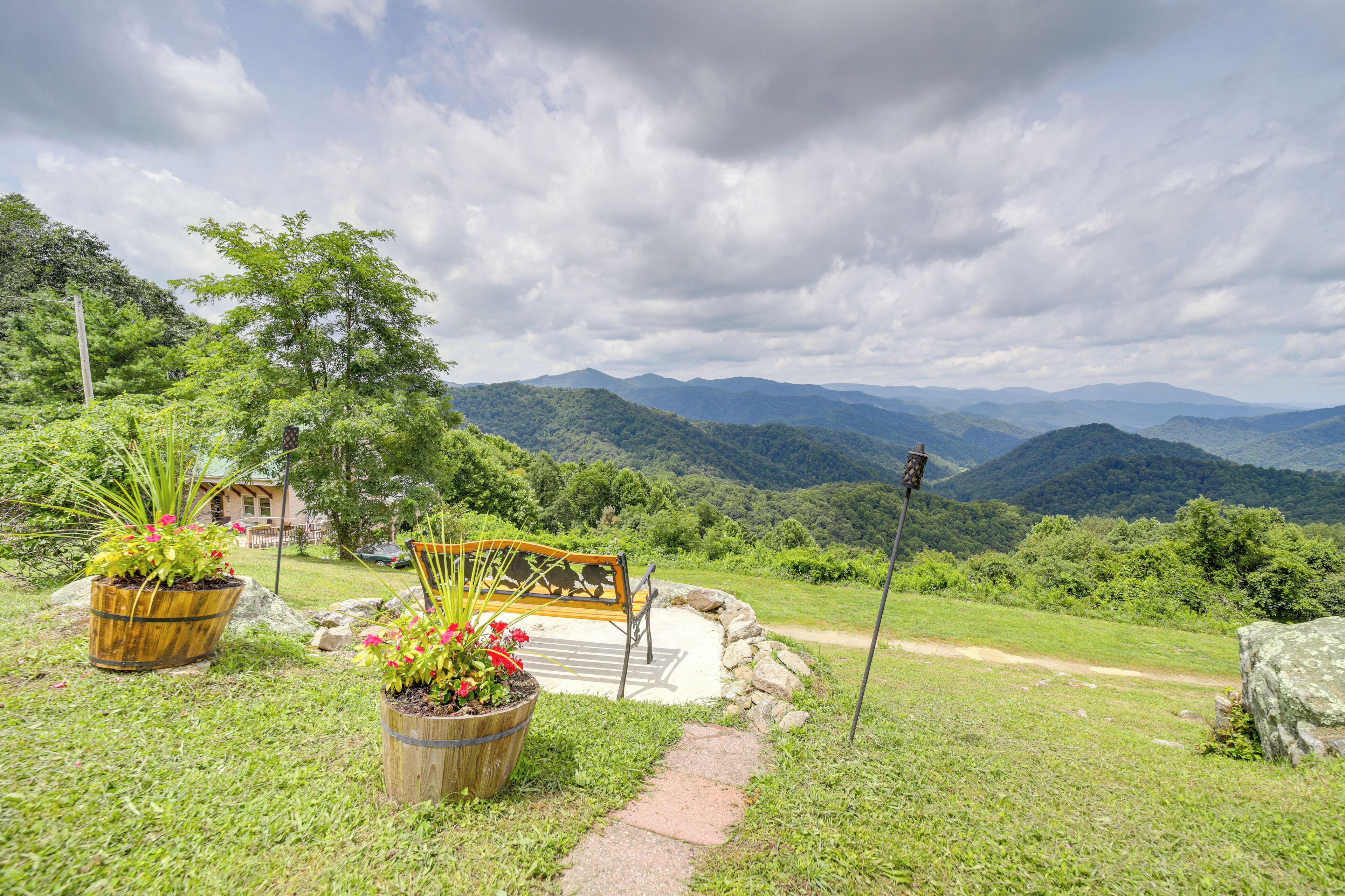 A scenic outdoor seating area with a wooden bench and potted plants, overlooking a mountainous landscape.