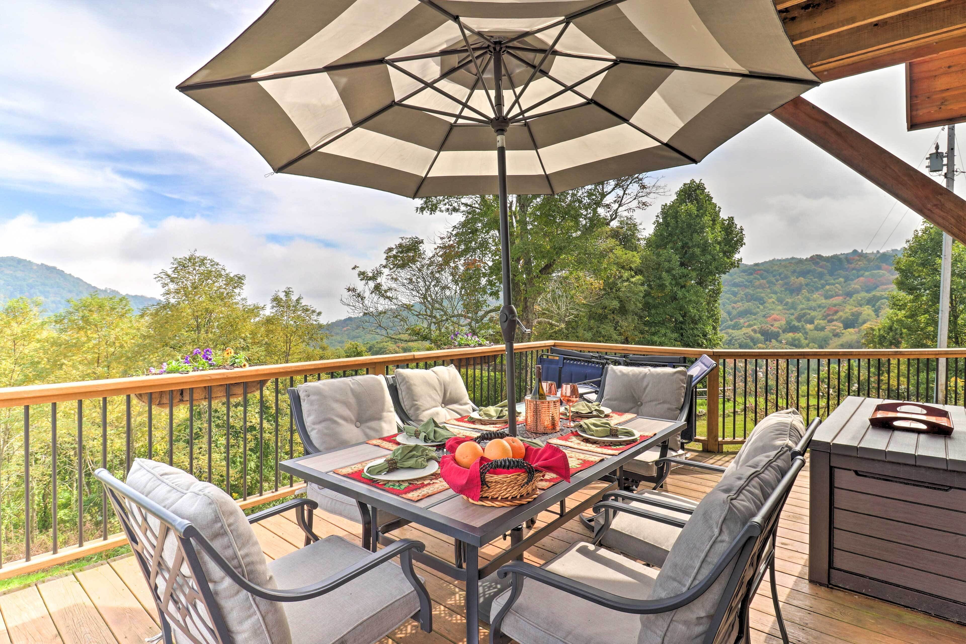A deck with a table set for dining, outdoor chairs, and a large umbrella.