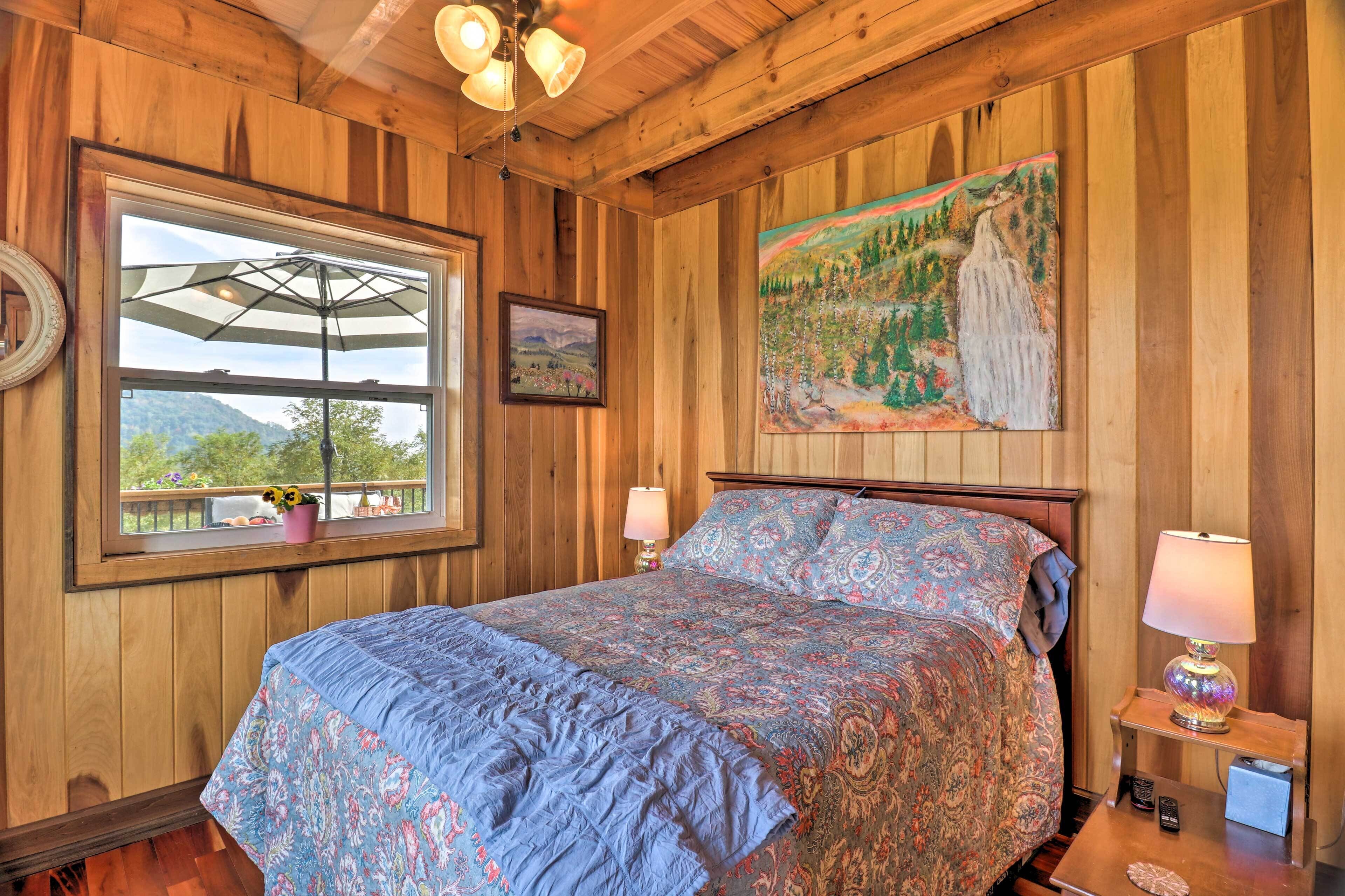 A wooden-paneled bedroom with a bed, a window with an umbrella, a painting, and a nightstand with a lamp.
