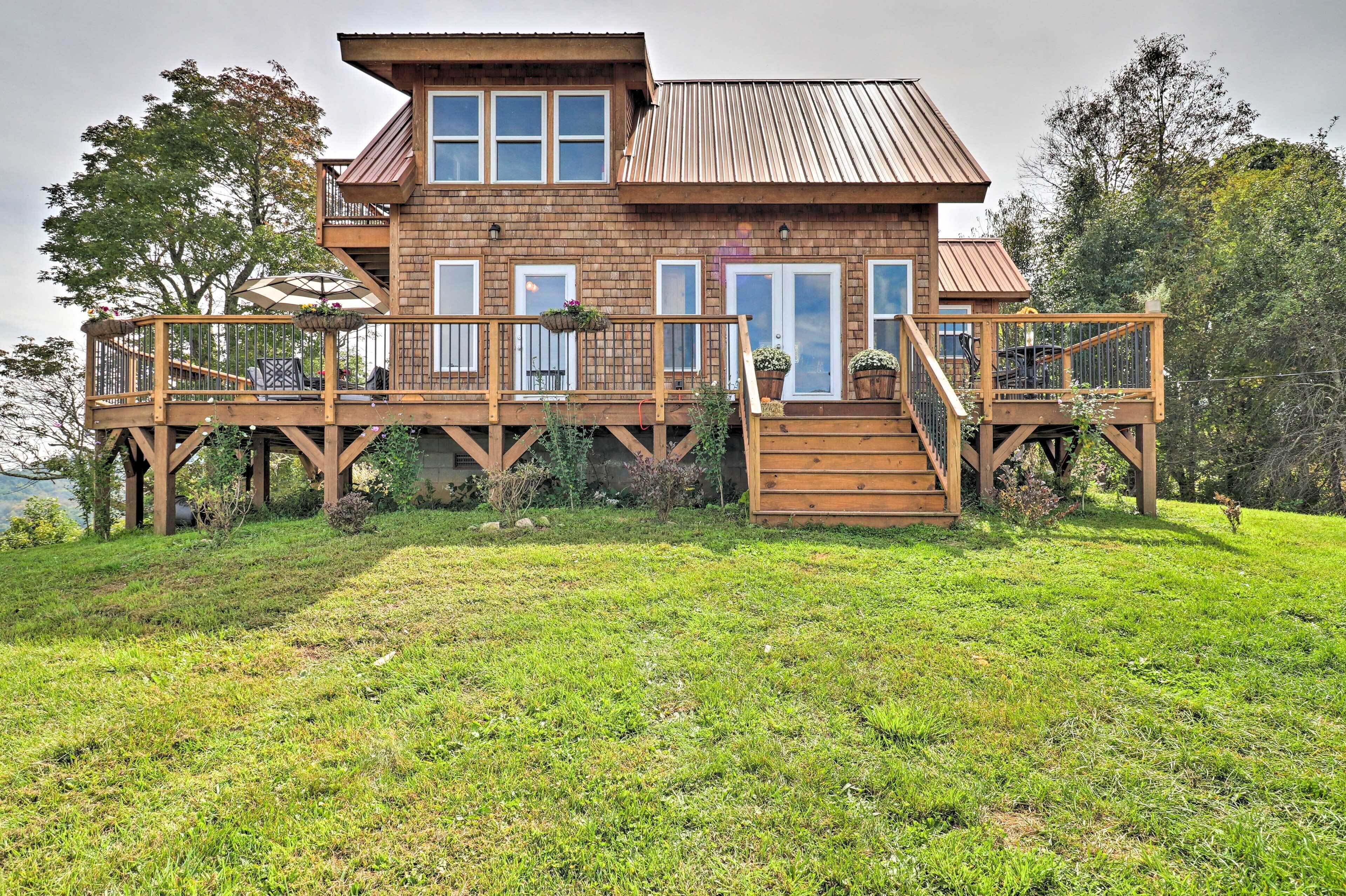 A two-story wooden house with a deck, large windows, and a view of the surrounding landscape.