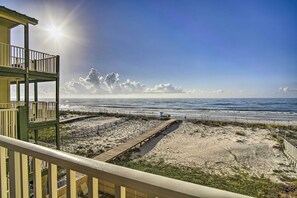 A beach view from a balcony with a wooden walkway leading to the shore, clear skies, and a calm sea.