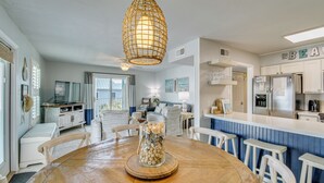 A kitchen with a wooden table, white chairs, a hanging light fixture, and a refrigerator. - Oceanfront Gulf Shores Condo ~ 2 Mi to The Hangout (Gulf Shores)
