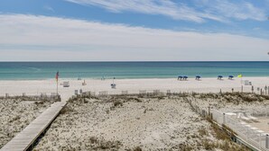 A beach with a wooden boardwalk, beach umbrellas, and a flag. - Oceanfront Gulf Shores Condo ~ 2 Mi to The Hangout (Gulf Shores)