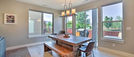 A spacious dining area with a wooden table and benches, large windows offering views of the outdoors, and a ceiling light fixture.