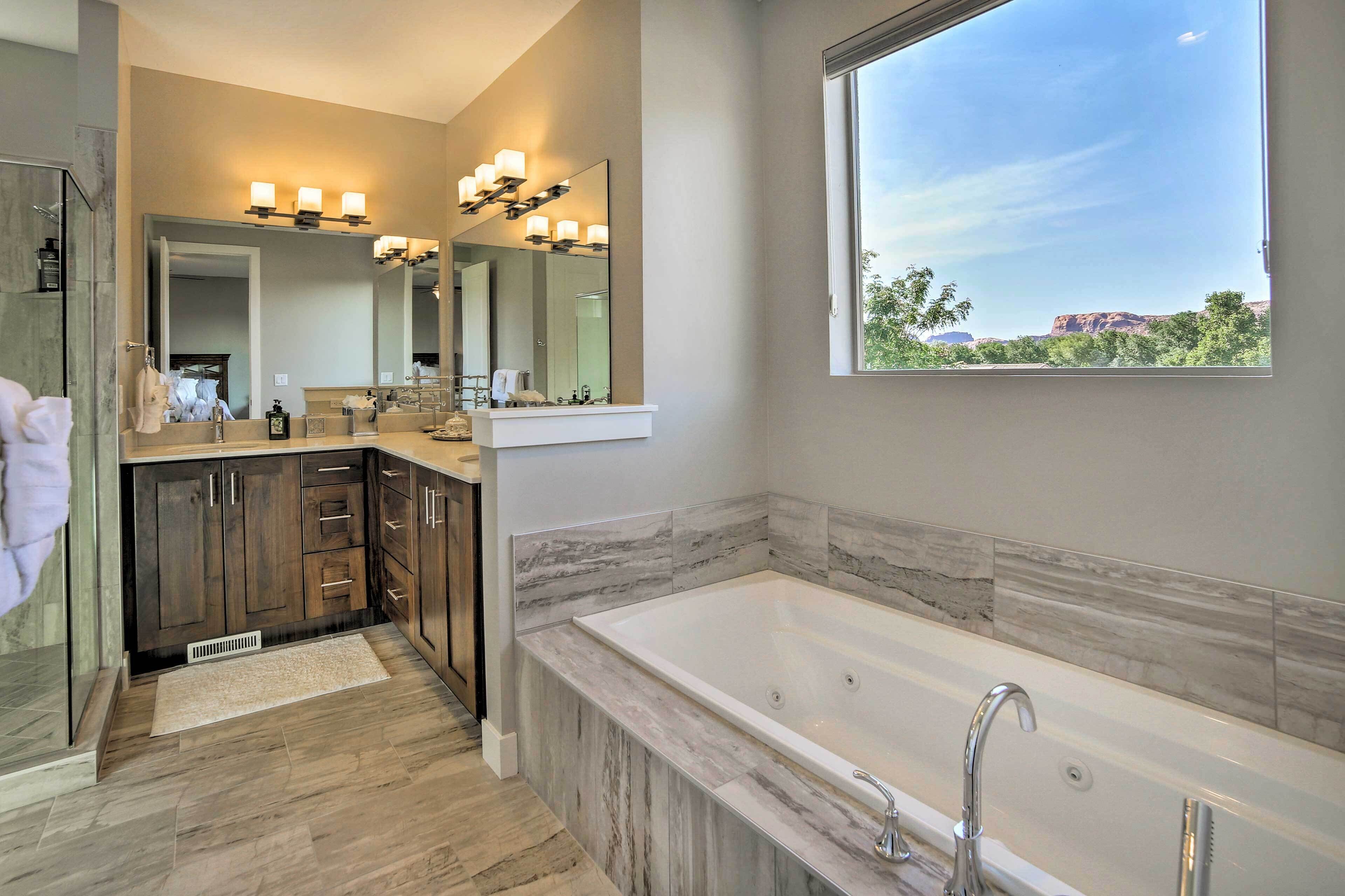 A modern bathroom with a large bathtub, a vanity with a mirror, and a window offering a view of the outdoors.