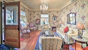A traditional living room with patterned wallpaper, wooden flooring, and classic furniture including a sofa, armchairs, and a coffee table. - Walk to Main St Action! Spacious Historic Retreat (Fredericksburg)
