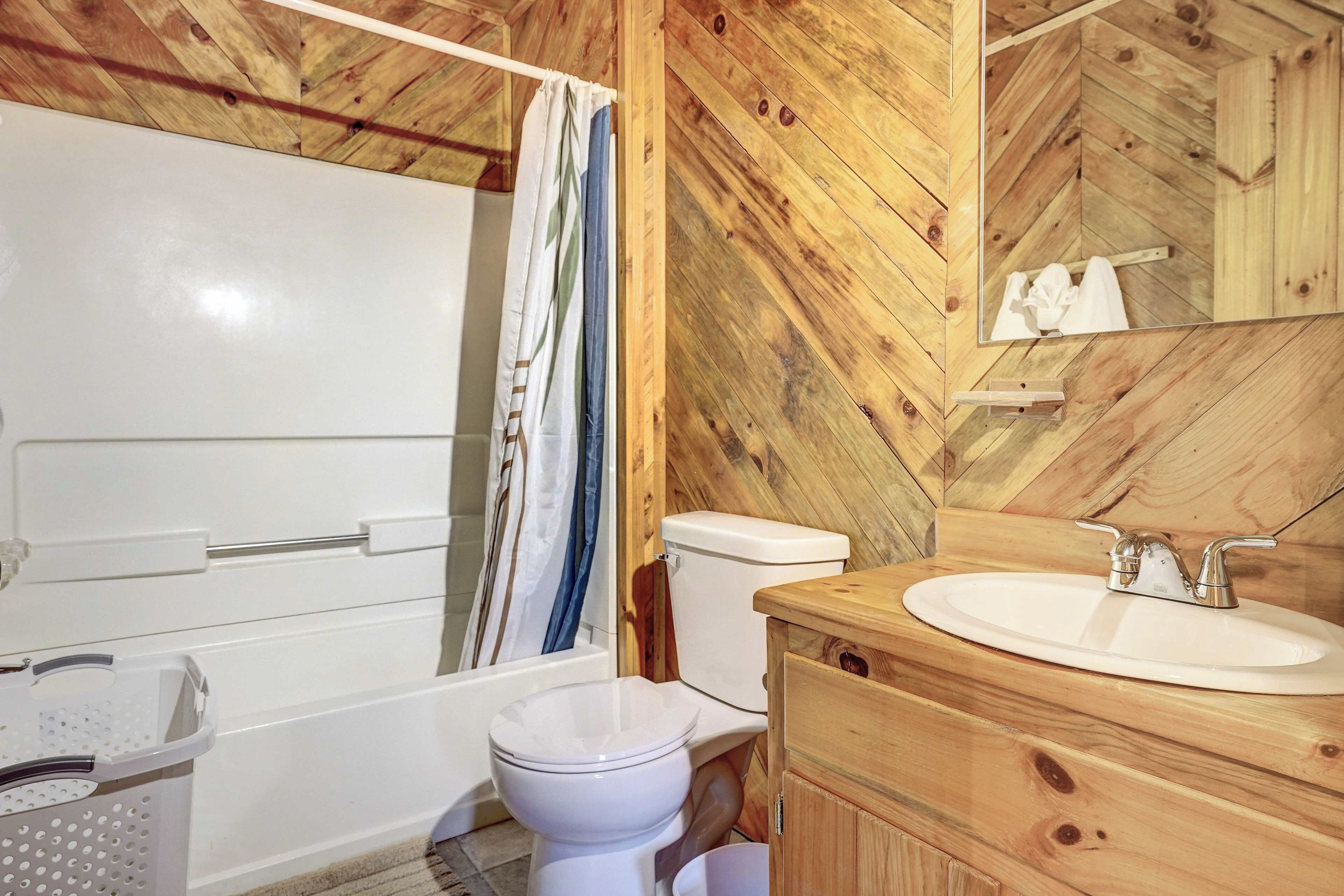 A bathroom with a wooden wall, a white toilet, a wooden vanity with a sink, and a shower curtain.