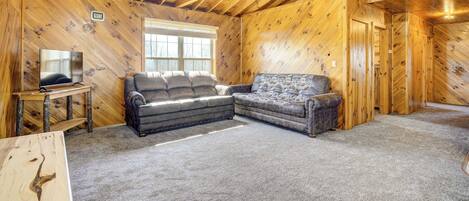 A log cabin interior with a wooden ceiling, a television on a wooden stand, two sofas, and a carpeted floor.