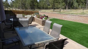 An outdoor patio with a glass table and chairs, surrounded by a brick wall and a wooden fence.