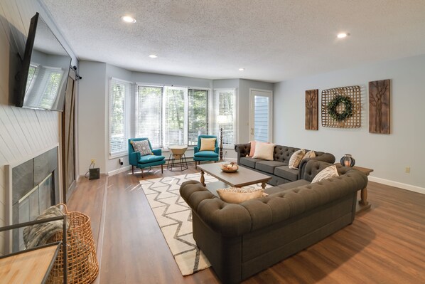 Un salon spacieux avec une cheminée, un grand canapé, deux fauteuils, une table basse et un tapis.