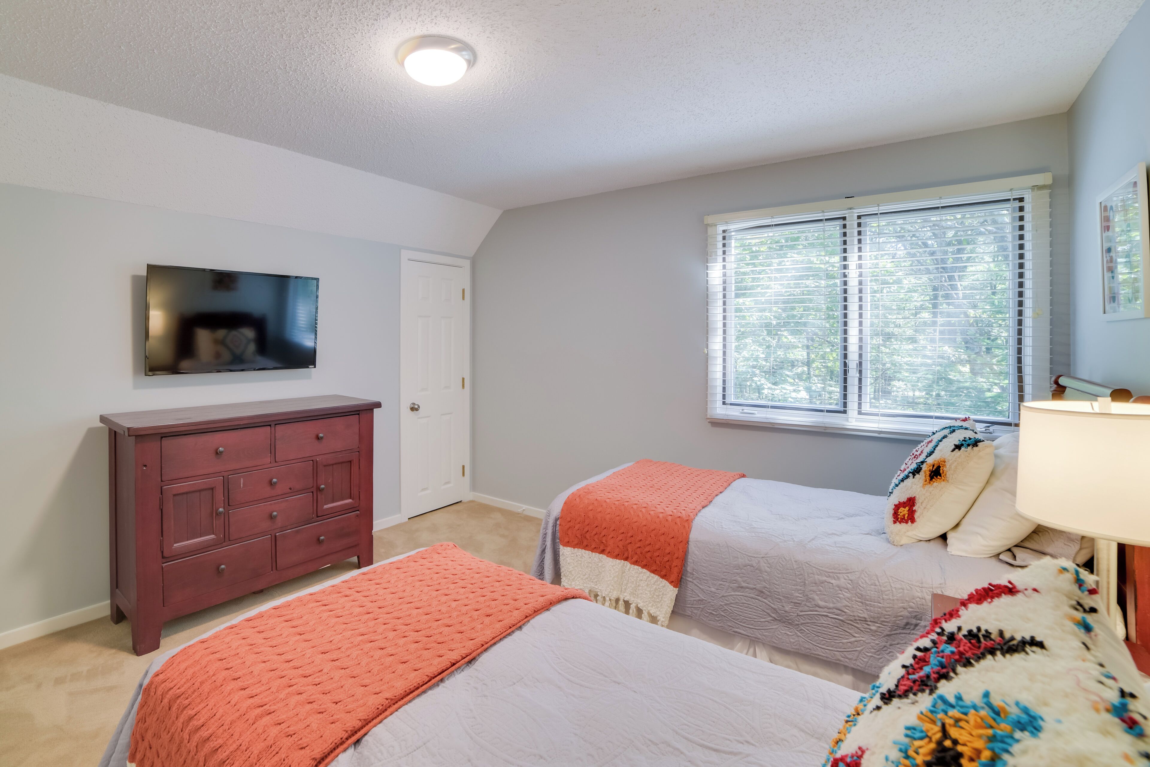 A bedroom with two beds, a dresser, a TV, and a window with blinds.