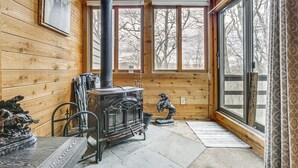 A cozy cabin interior with a wood-burning stove, a dining table, chairs, and a statue. - Pristine Resort Townhome 2 Mi to Seven Springs Mtn (Champion)