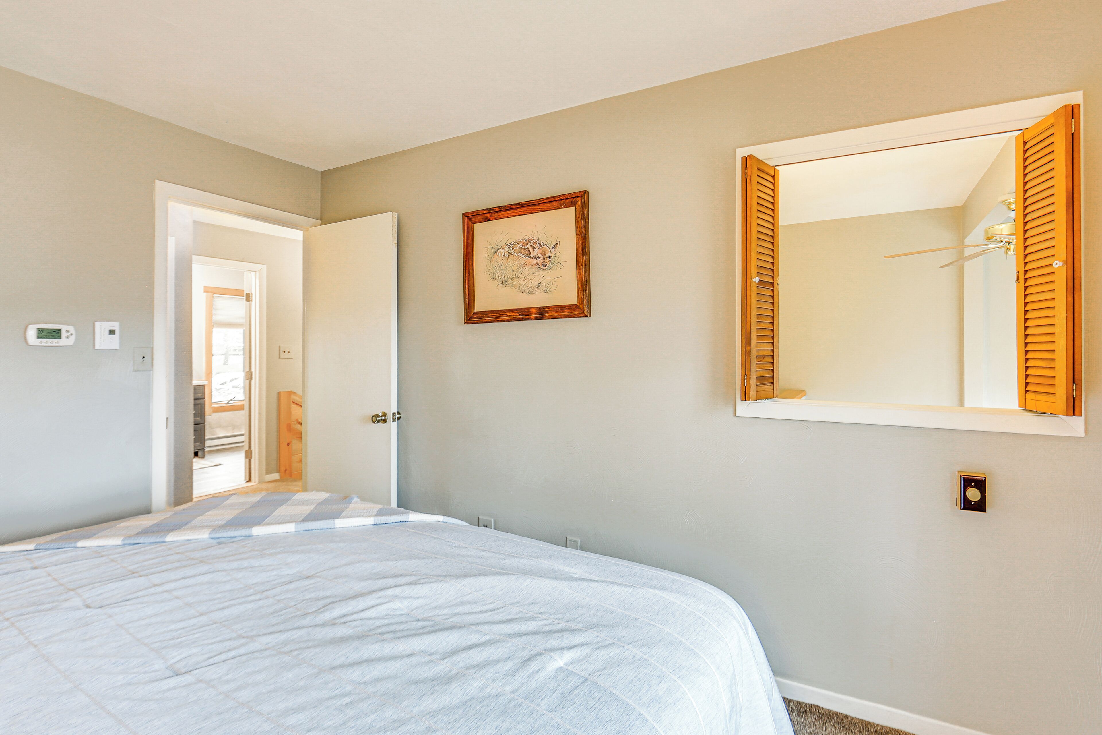 Quarto com cama, porta para outro cômodo, quadro pendurado na parede e ventilador de teto.