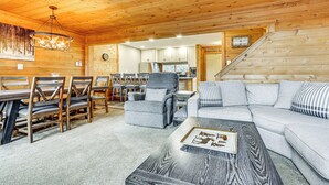 A cozy cabin interior with a dining area, a sofa, and a staircase leading to a kitchen. - Pristine Resort Townhome 2 Mi to Seven Springs Mtn (Champion)