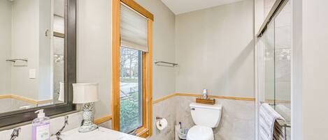 A bathroom with a marble vanity, a toilet, a glass shower enclosure, and a window with blinds.