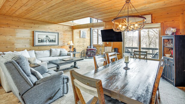 A cozy log cabin interior with a wooden dining table, gray sofa, and a large window overlooking a snowy landscape. - Pristine Resort Townhome 2 Mi to Seven Springs Mtn (Champion)