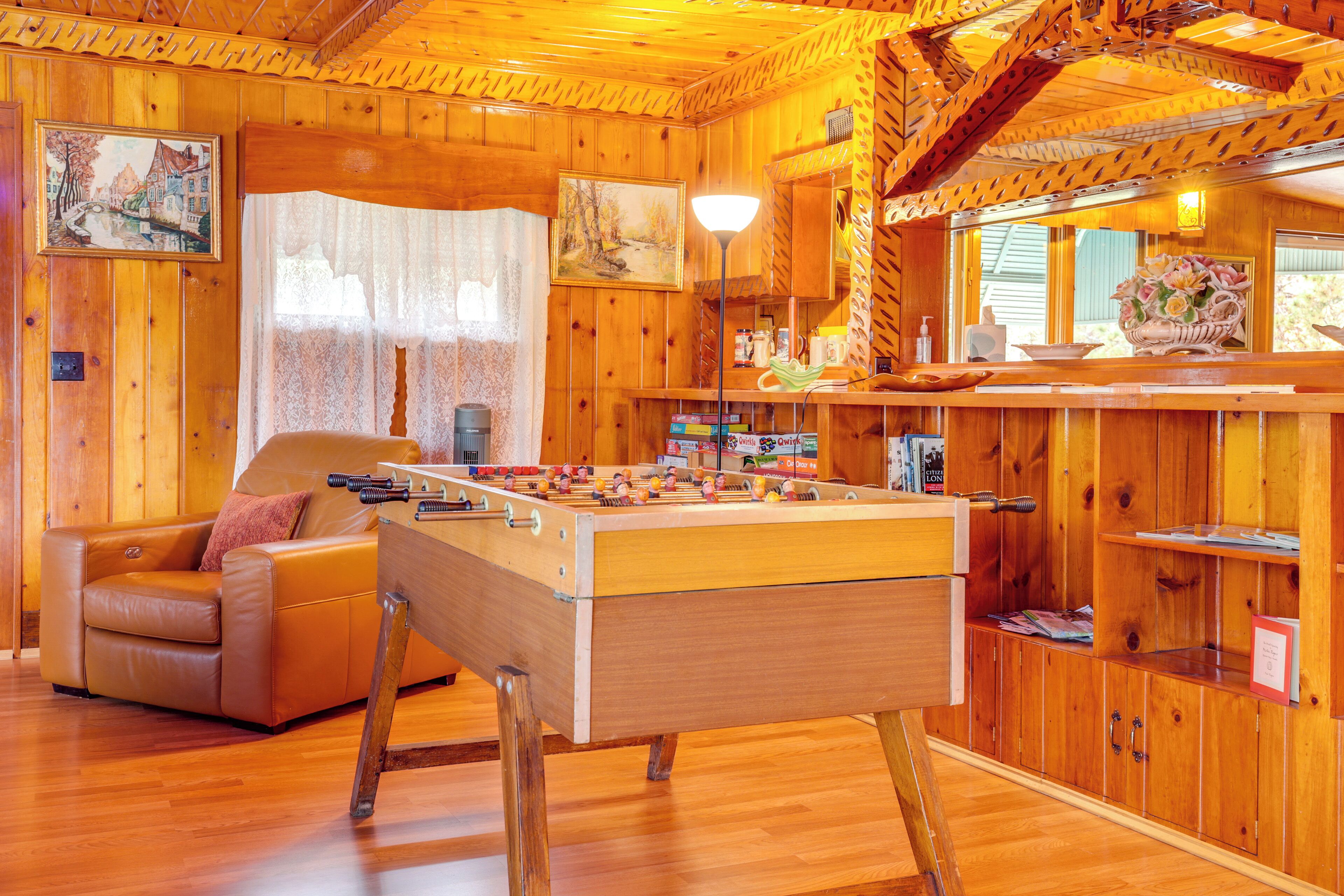 Una habitación acogedora de madera con una mesa de fútbol de mesa, un sofá y una mesa de comedor con sillas.