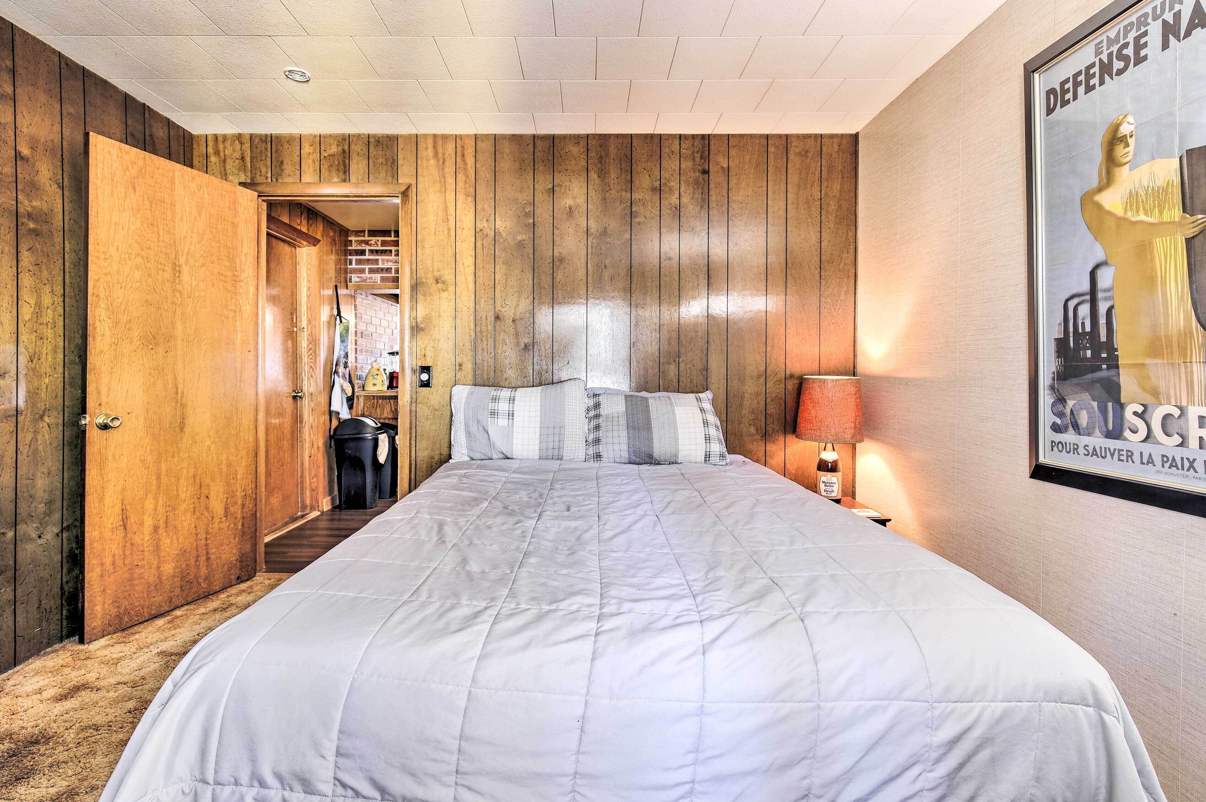 Un dormitorio con pared de paneles de madera, una cama con edredón blanco, una mesita de noche con lámpara y un cartel en la pared.
