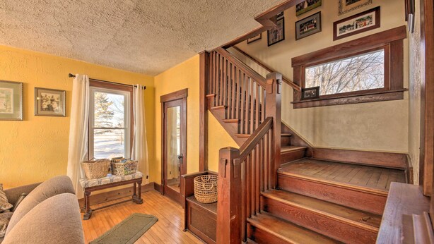 Un salón acogedor con una escalera de madera, un banco y una ventana con vistas a árboles.
