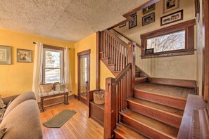 A cozy living room with a wooden staircase, a bench, and a window with a view of trees. - Quaint & Family-friendly Watertown Farmhouse! (Watertown)