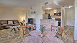 Una sala moderna con sofá, mesa de centro y televisor, un comedor con mesa y sillas, y una cocina con electrodomésticos.
