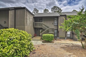 A residential building with a grey exterior, a small front yard with a trimmed bush, and a staircase leading to a balcony.