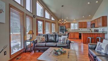 A spacious living room with a leather sofa, a coffee table with pinecones, and large windows with blinds.