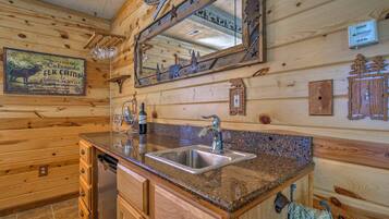 A wooden cabin interior with a granite countertop sink, wooden cabinets, and a large mirror reflecting the room.
