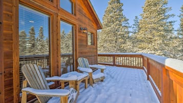 A wooden cabin with a snow-covered deck and two Adirondack chairs.