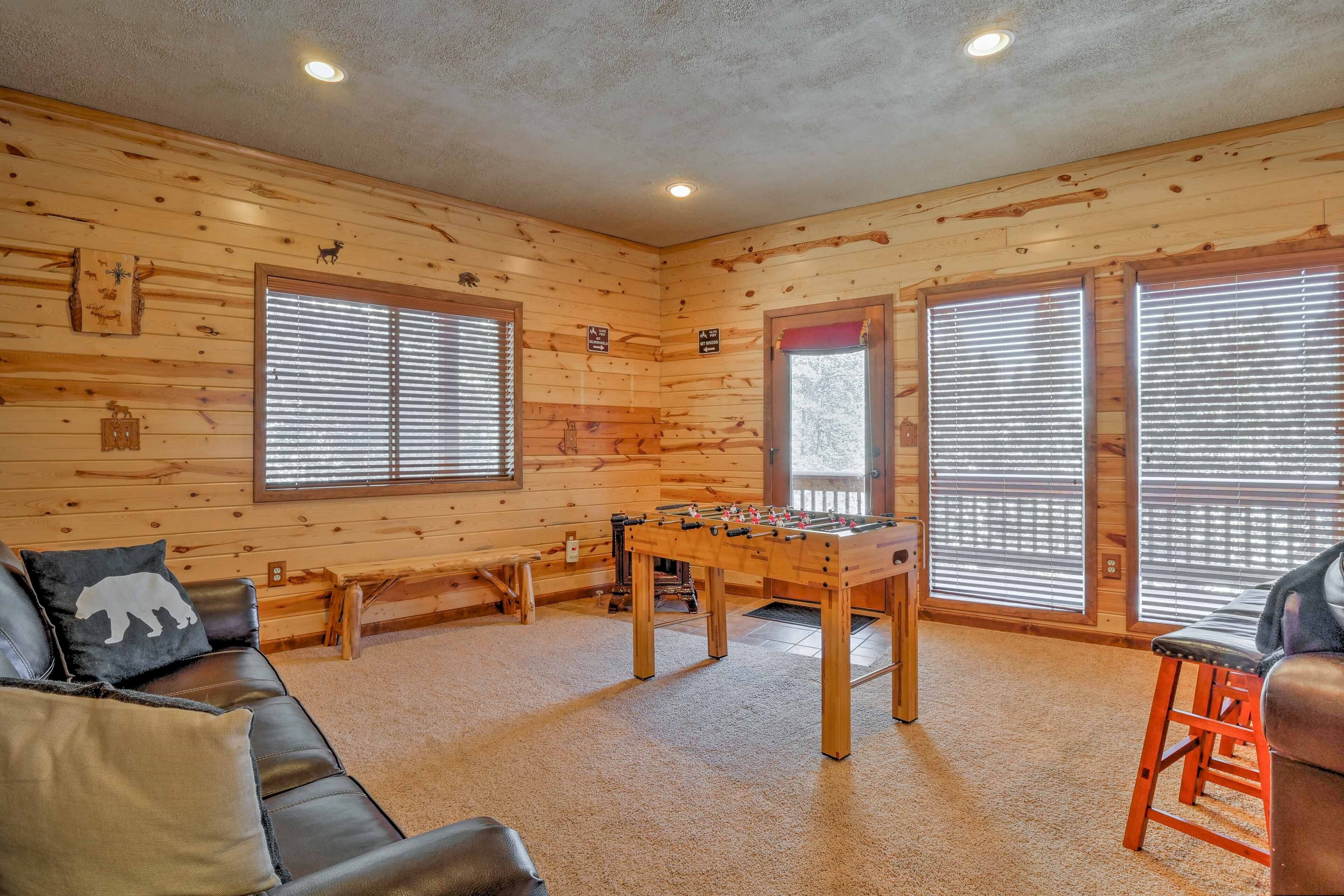 A cozy room with wooden walls, a foosball table, a sofa, and a window with blinds.
