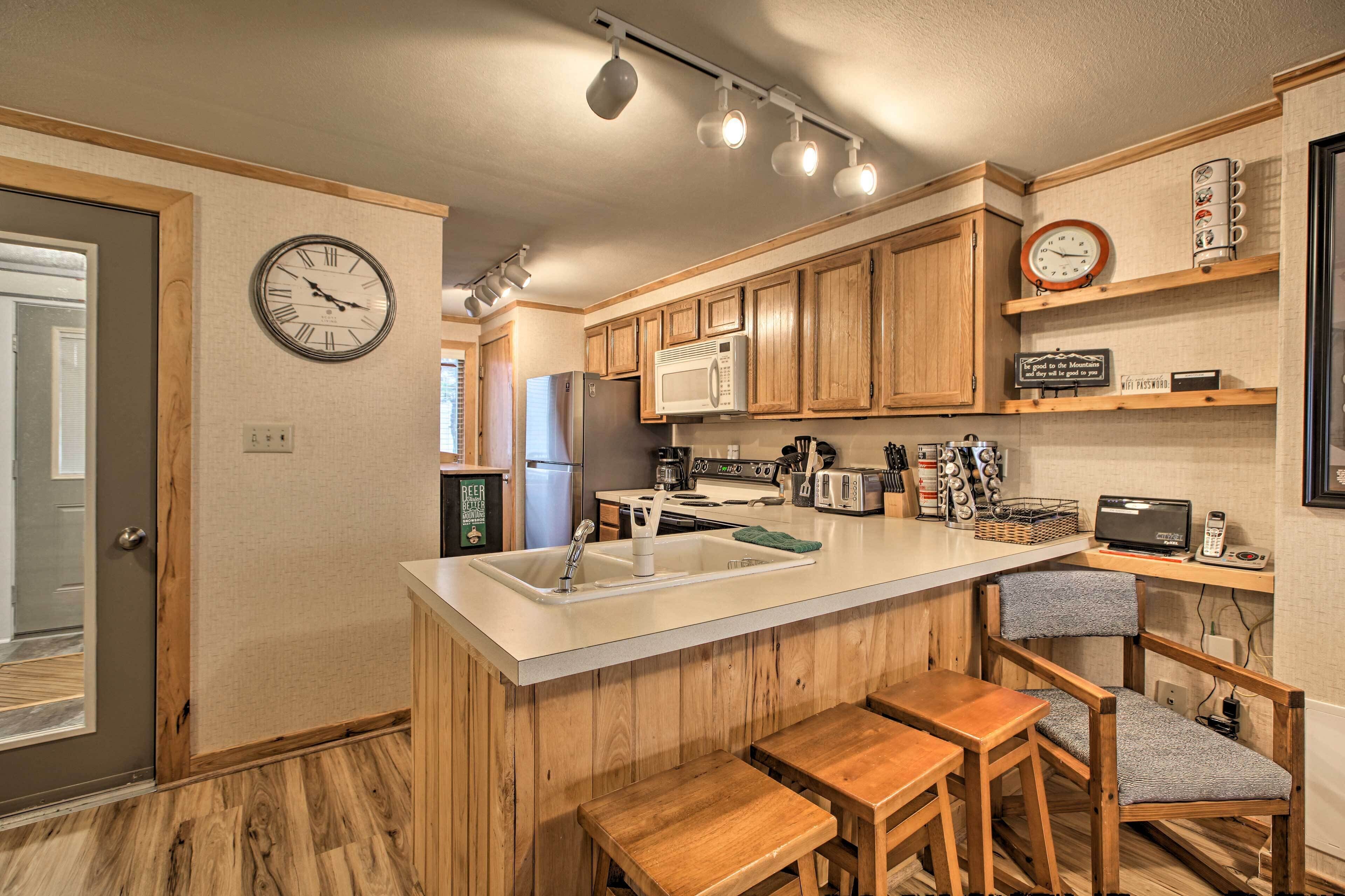 A modern kitchen with wooden cabinets, a central island with seating, a microwave, and a clock on the wall.
